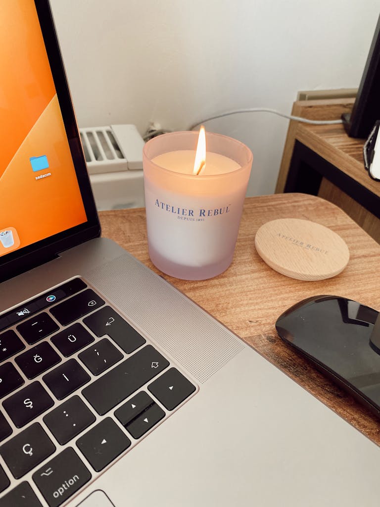 An inviting workspace featuring a lit candle beside a laptop and mouse on a wooden desk.
