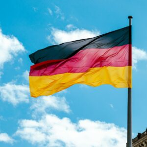 Vibrant German flag waving on a flagpole against a bright blue sky with clouds.